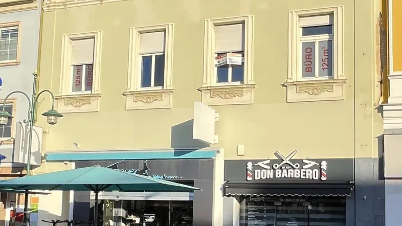 Historisches Gebäude mit Geschäften im Erdgeschoss und Büros in den oberen Etagen an einer belebten Straße.