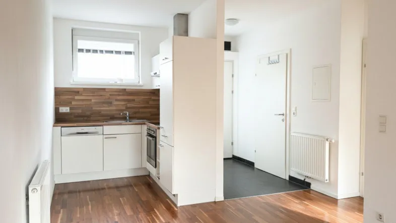 Helle, offene Küche mit Holzoptik-Arbeitsplatte und Parkettboden, integriert in einen Wohnbereich.