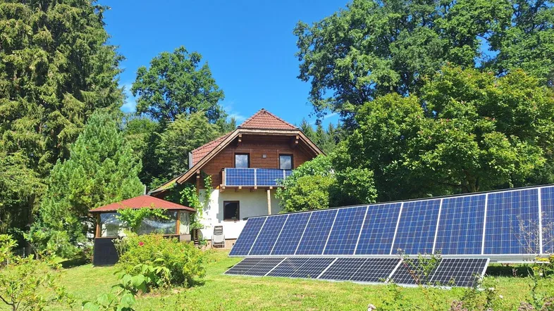 Freistehendes Haus mit großem Garten, Solaranlage und Gartenlaube unter blauem Himmel.