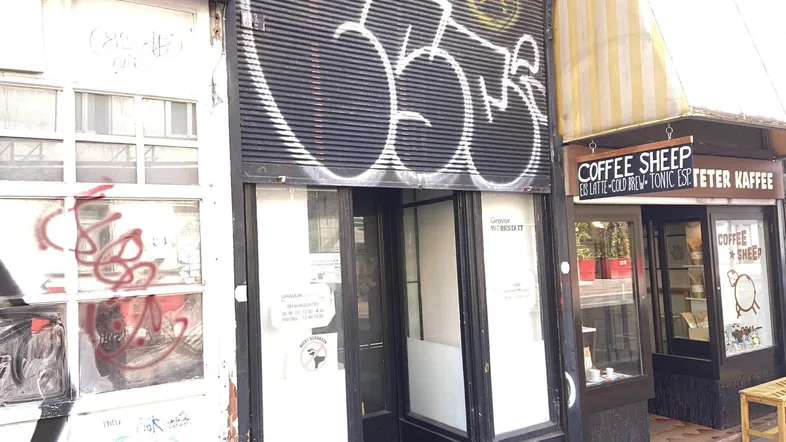 Fassade eines Geschäfts mit Rollladen und Graffiti, daneben ein weiteres Geschäft mit Markise.