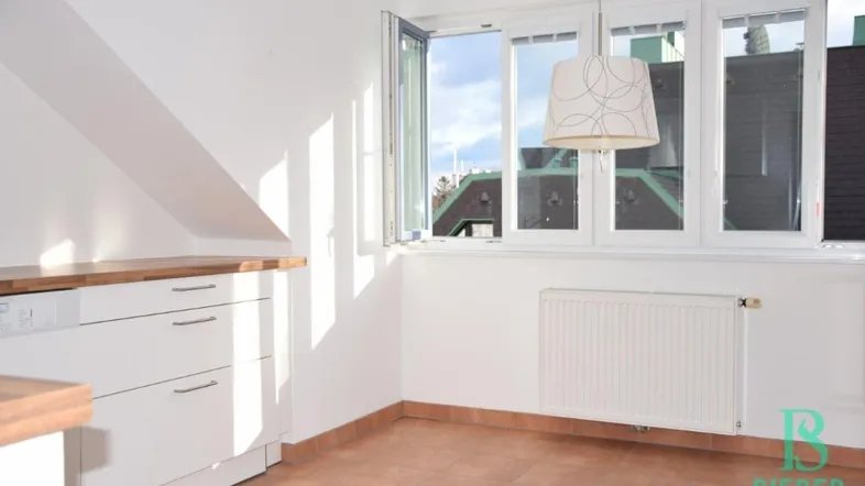 Helle Küche mit weißen Schränken, Holztheke, Fliesenboden und Dachschrägenfenster.