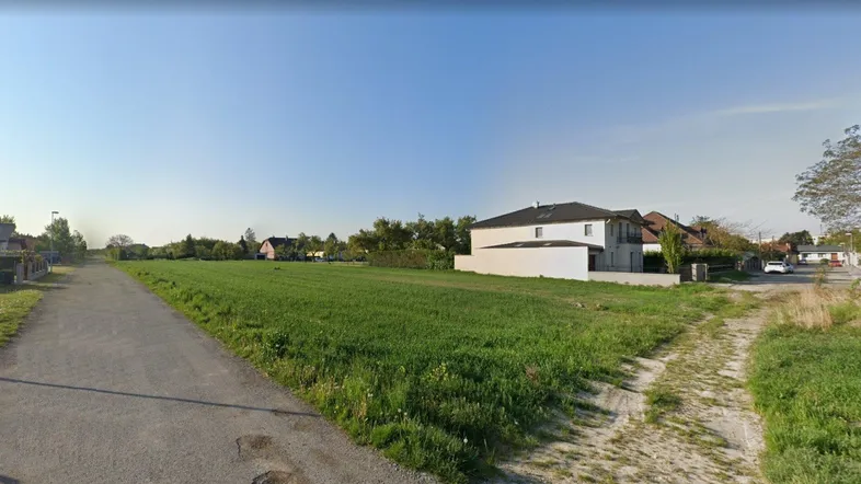 Weitläufiges grünes Feld mit Wohnhäusern im Hintergrund unter klarem Himmel.