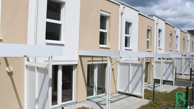 Reihenhäuser mit modernen Fassaden und kleinen Terrassen im Erdgeschoss, umgeben von Grünflächen.