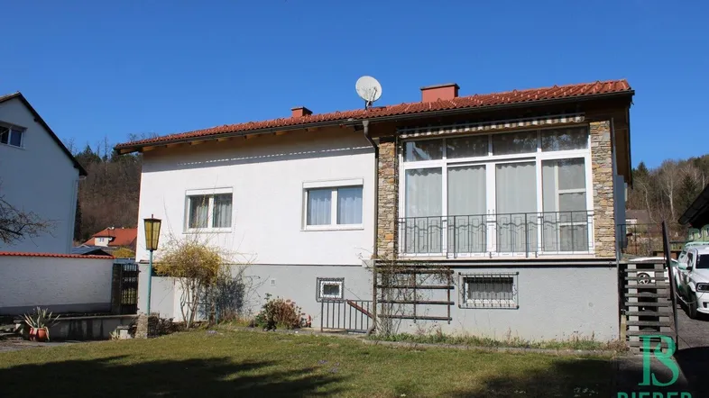 Einfamilienhaus mit weißer Fassade, rotem Ziegeldach und kleinem Vorgarten.
