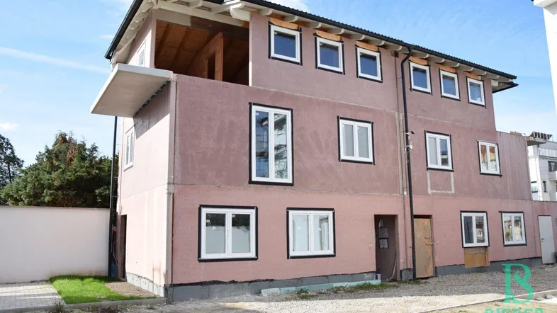 Gebäude im Rohbauzustand mit rosafarbener Fassade und vielen Fenstern unter blauem Himmel.