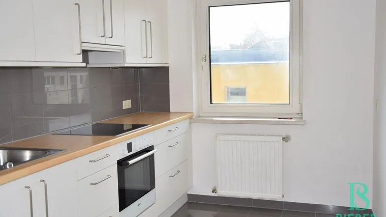 Helle Küche mit weißen Schränken, Holz-Arbeitsplatte und Fenster, ausgestattet mit modernen Geräten.