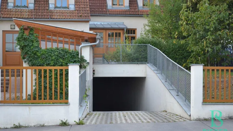 Einfahrt zu einer Tiefgarage mit Rampe und Geländer, umgeben von einem Wohngebäude mit Holzelementen.