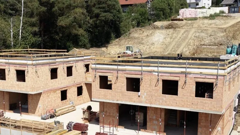 Baustelle mit mehreren im Bau befindlichen Reihenhäusern in hügeliger Landschaft.