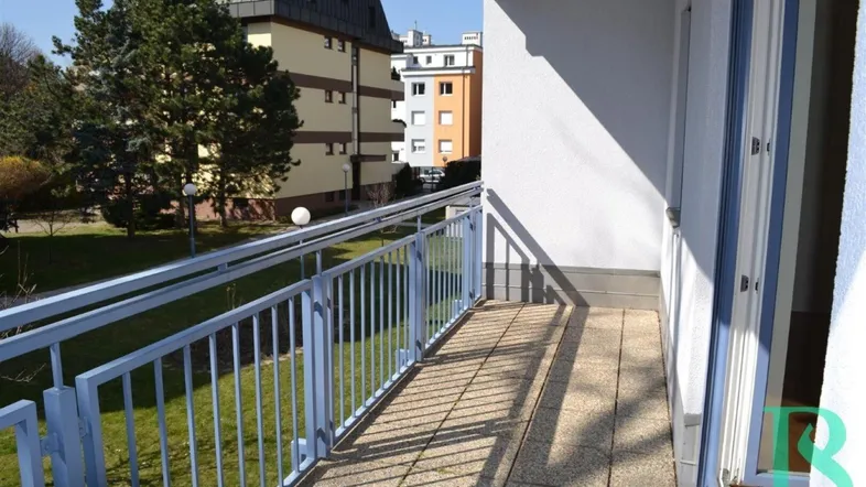 Heller Balkon mit Fliesenboden und blauem Geländer, bietet Blick auf die umliegenden Gebäude und Grünflächen.