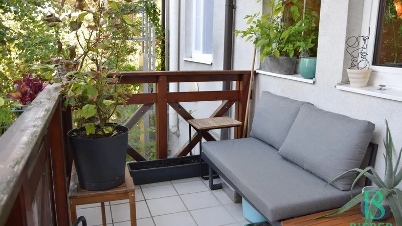 Gemütlicher Balkon mit Fliesenboden, bequemer Sitzgelegenheit und vielen Pflanzen für eine grüne Oase.