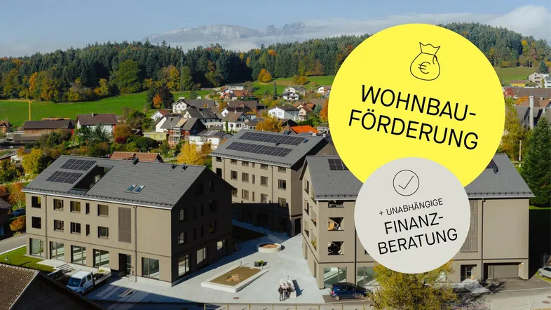 Moderne Mehrfamilienhäuser mit Photovoltaikanlagen in ländlicher Umgebung, umgeben von grünen Hügeln und Bergen.