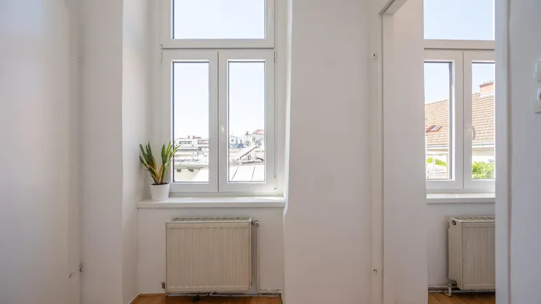 Heller Flur mit Holzboden, Heizkörper und Blick auf die Dächer der Stadt.