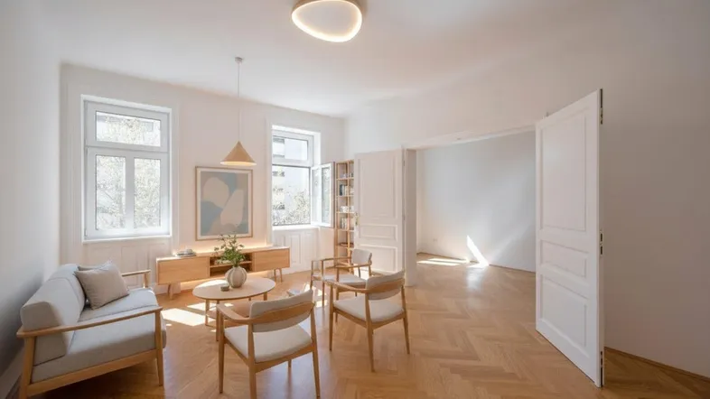 Helles Wohnzimmer mit Fischgrätparkett, modernen Möbeln und hohen Decken, das zu einem weiteren Raum führt.
