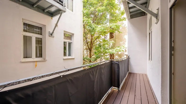 Schmaler Balkon mit Holzboden und Blick in einen grünen Innenhof.