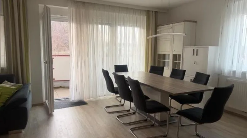 Heller Wohn- und Essbereich mit modernem Esstisch, Laminatboden und Zugang zum Balkon.