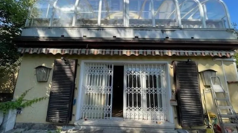 Gebäude mit gelber Fassade, Sicherheitsgittern und einem verglasten Wintergarten auf dem Dach.