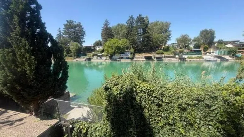 Panoramablick auf den türkisfarbenen Kanal mit üppiger Vegetation am Ufer unter blauem Himmel.