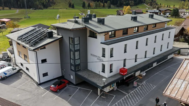 Luftaufnahme des modernen Wohn- und Geschäftshauses mit Photovoltaikanlage und Parkplätzen in ländlicher Umgebung.