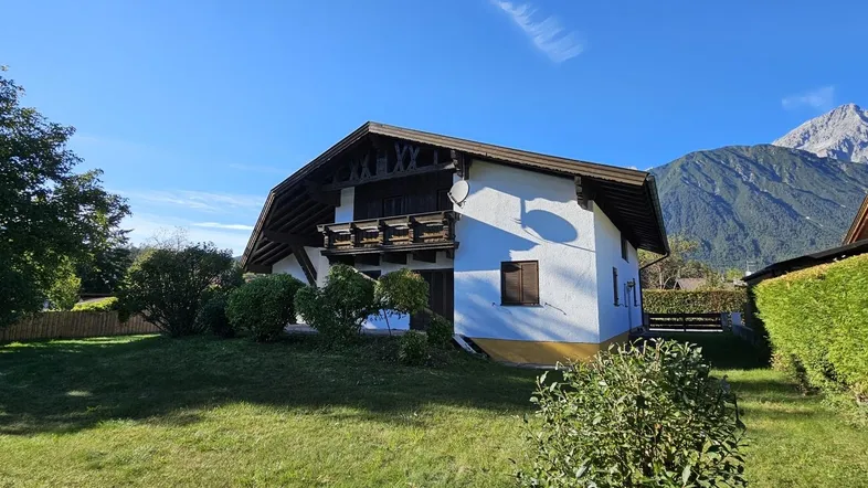 Alpines Haus mit weißer Fassade, Holzbalkonen und Bergblick an einem sonnigen Tag.