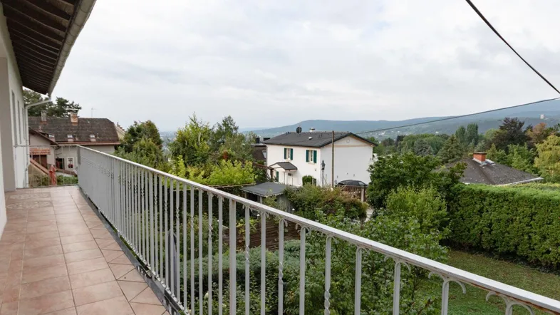 Langer Balkon mit Fliesenboden und Blick auf die grüne Umgebung und die Berge.