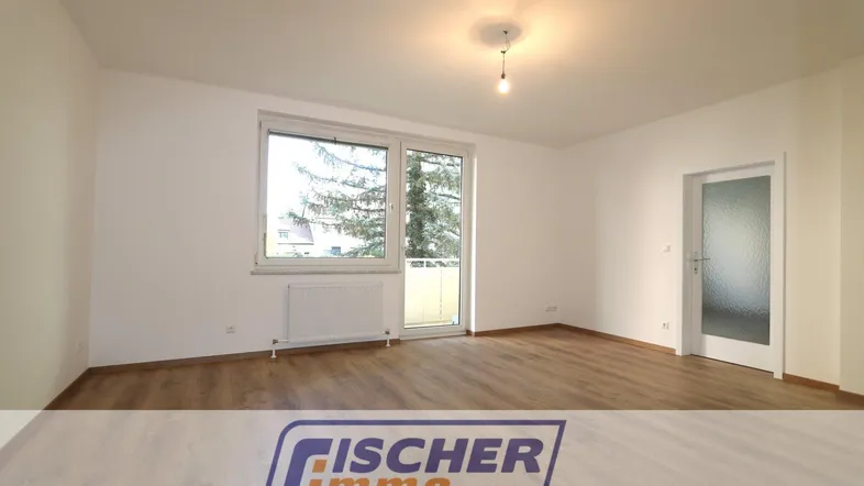 Heller Wohnraum mit Laminatboden, weißen Wänden und Zugang zu einem Balkon.