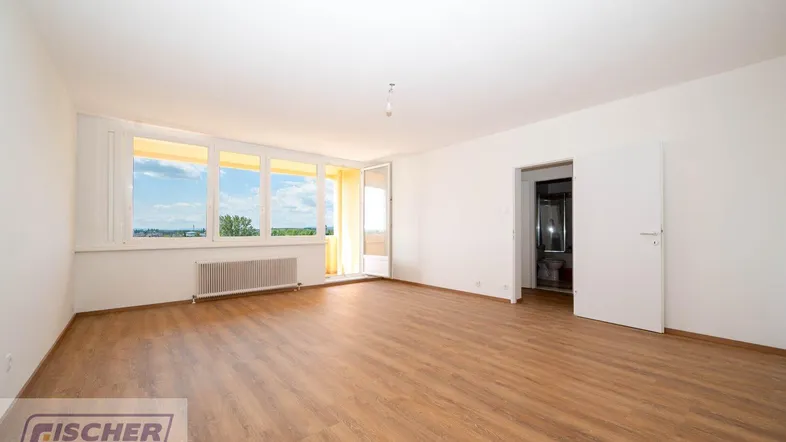 Helles, leeres Zimmer mit Laminatboden, großen Fenstern und Zugang zu einem Balkon.