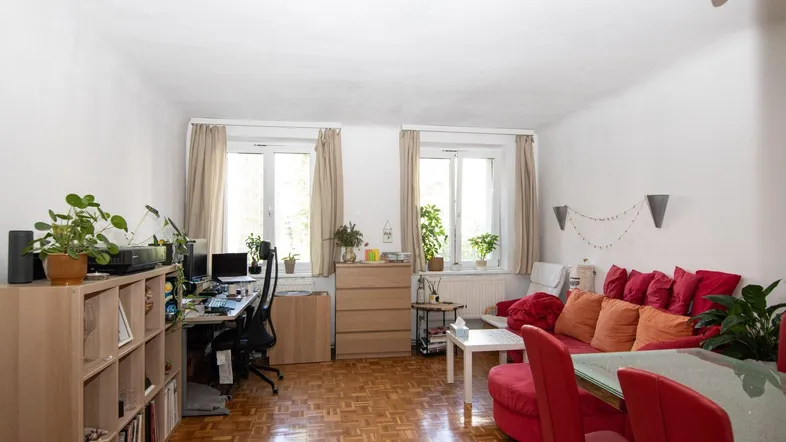 Helles Wohn- und Esszimmer mit Parkettboden, rotem Sofa und integriertem Arbeitsbereich.
