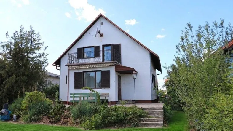 Freistehendes Einfamilienhaus mit weißer Fassade, Satteldach und einem gepflegten Vorgarten.