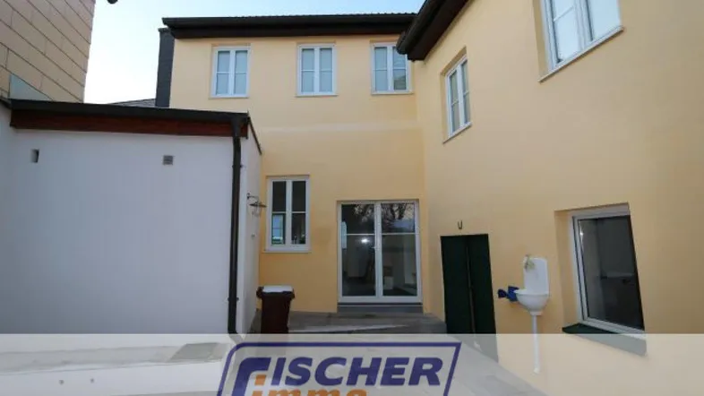 Außenansicht eines Gebäudes mit gepflastertem Hof und mehreren Fenstern.