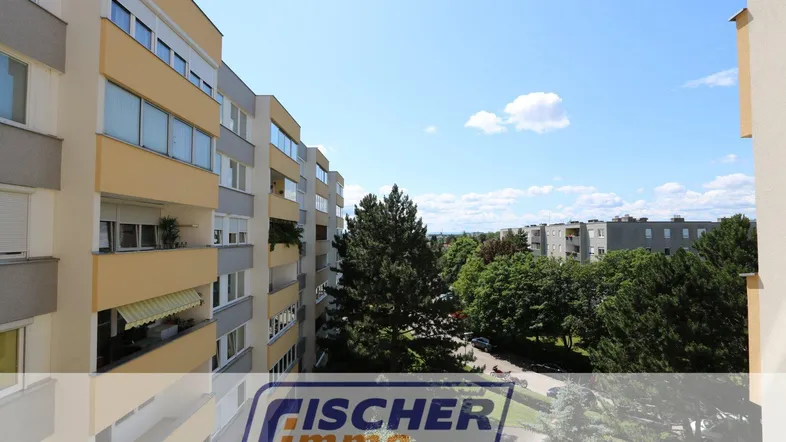 Blick von einem oberen Stockwerk auf die Fassade eines Mehrfamilienhauses mit Balkonen und grüner Umgebung.