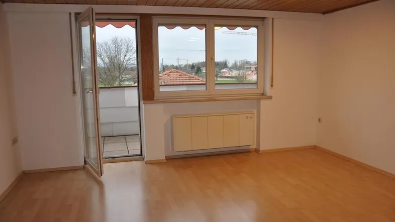 Helles Zimmer mit Holzbalkendecke, Laminatboden und Zugang zu einem kleinen Balkon.