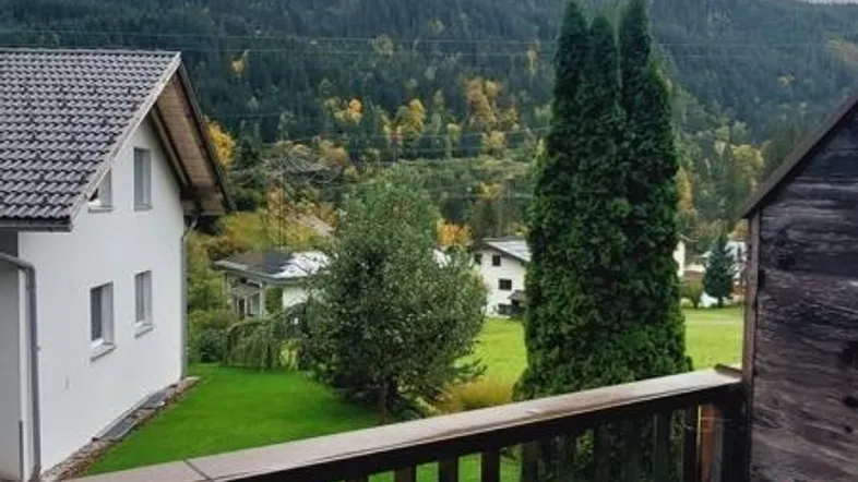 Blick von der Terrasse auf den Garten und die umliegende Berglandschaft unter bewölktem Himmel.