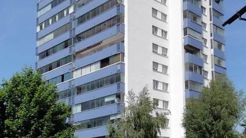 Hohes Wohngebäude mit vielen Etagen und blauen Balkonen unter blauem Himmel.