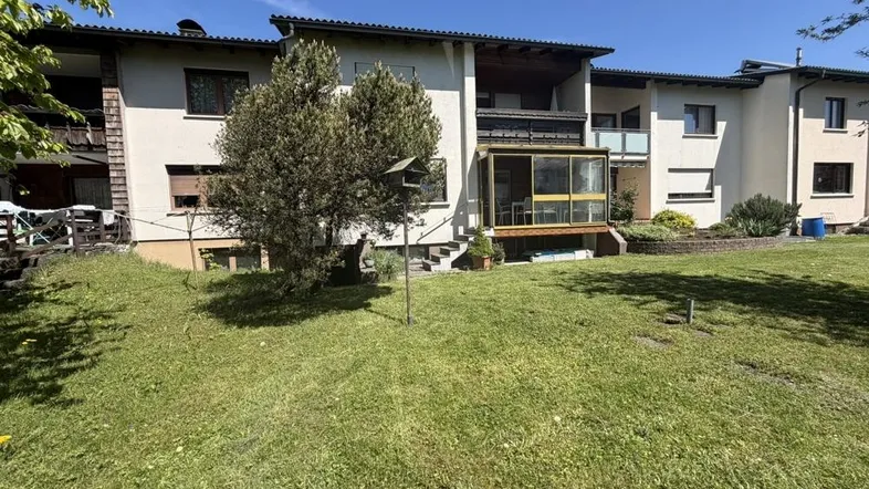 Mehrfamilienhaus mit großem Garten und Balkonen an einem sonnigen Tag.