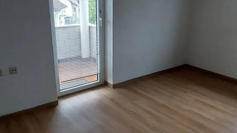 Helles Zimmer im Dachgeschoss mit Laminatboden und Zugang zu einem kleinen Balkon.