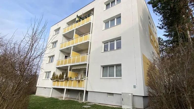 Mehrfamilienhaus mit weißer Fassade, gelben Balkonen und umgebender Grünfläche.