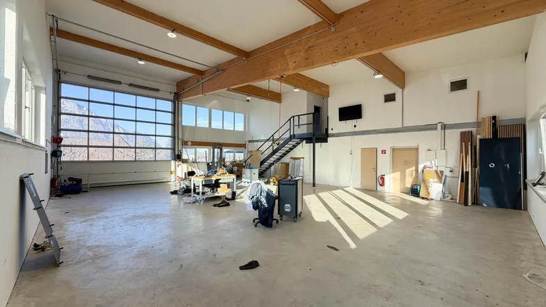 Geräumige Halle mit hohen Decken, Holzbalken und großen Fenstern, die viel Tageslicht hereinlassen und Bergblick bieten.