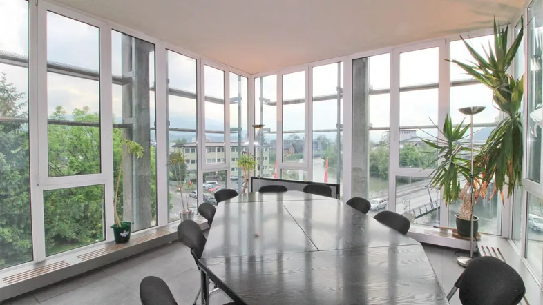 Moderner Konferenzraum mit großem Tisch, umgeben von raumhohen Fenstern und Blick auf die Stadt und Natur.