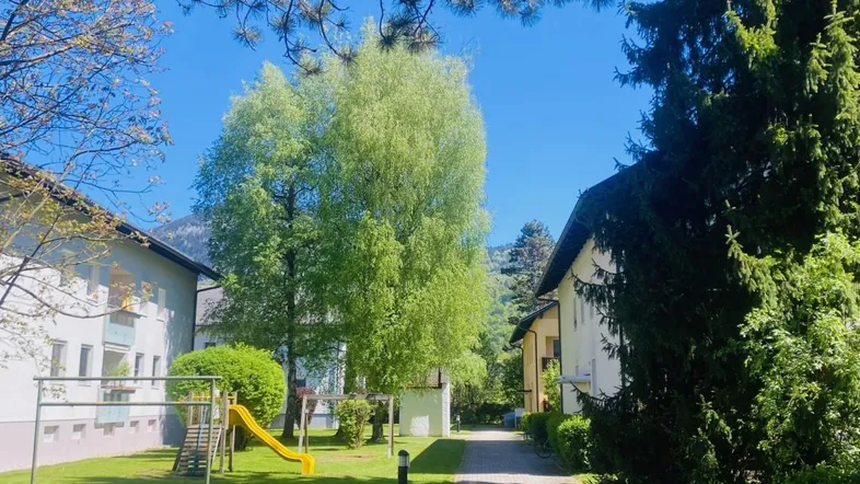 Grüne Außenanlage mit Spielplatz, Bäumen und Gehwegen zwischen den Wohngebäuden.