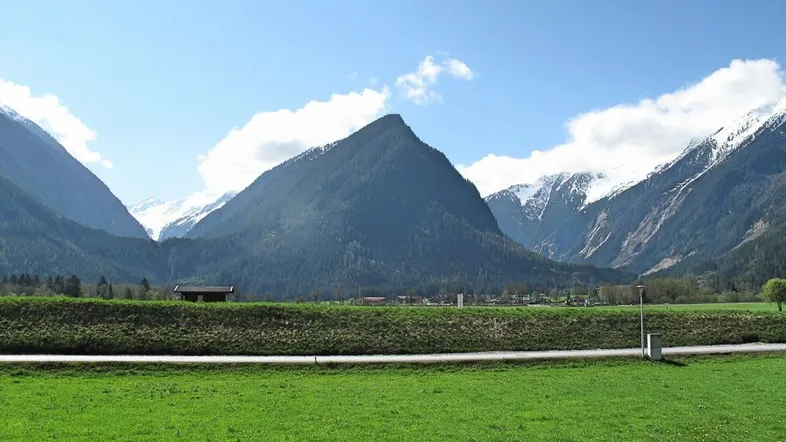 Weitläufige grüne Wiesen mit beeindruckendem Bergpanorama und schneebedeckten Gipfeln im Hintergrund.
