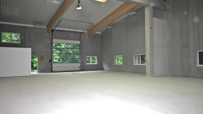 Geräumige, leere Lagerhalle mit hohen Decken, Betonwänden und großem Rolltor mit Fenstern.