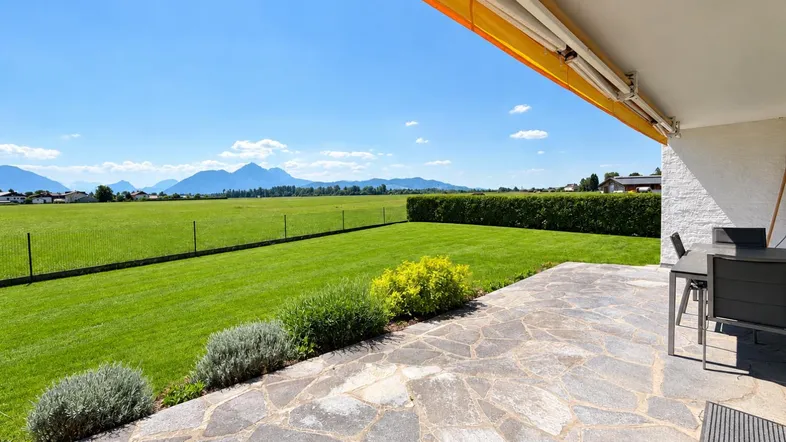Große Terrasse mit Steinplatten, angrenzendem Garten und weitem Bergblick unter einer Markise.