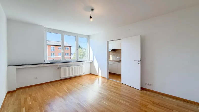 Helles Wohnzimmer mit Parkettboden und Fensterblick auf ein gegenüberliegendes Gebäude.