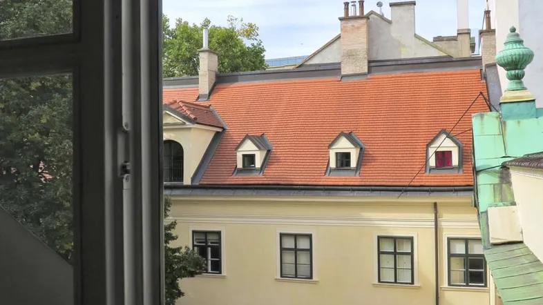 Blick aus dem Fenster auf ein historisches Gebäude mit roten Dächern und Gauben.