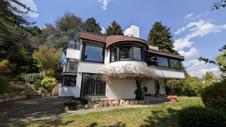 Modernes Haus mit geschwungenen Formen, großen Fenstern und umgebender Natur.