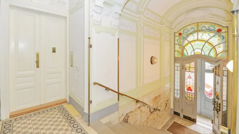 Prächtiges Treppenhaus mit kunstvollen Stuckverzierungen, Buntglasfenstern und historischen Fliesen.