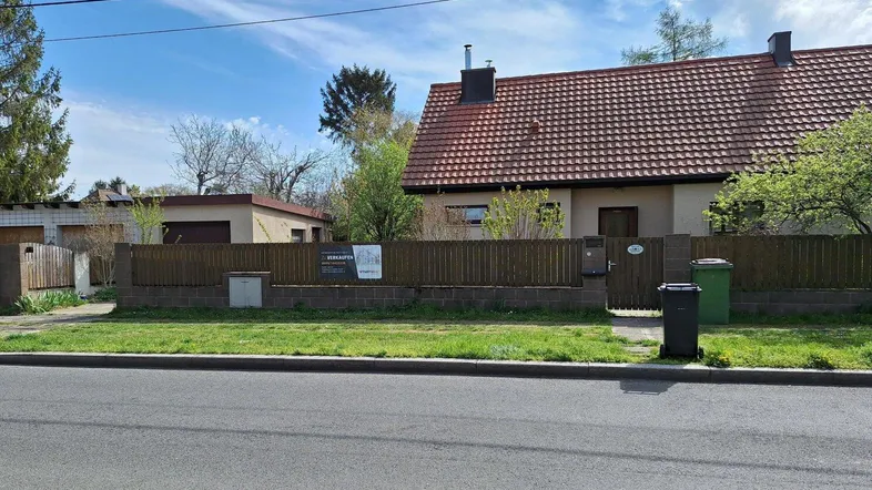 Vorderansicht des Hauses mit Vorgarten, Zaun und Garagenzufahrt unter blauem Himmel.