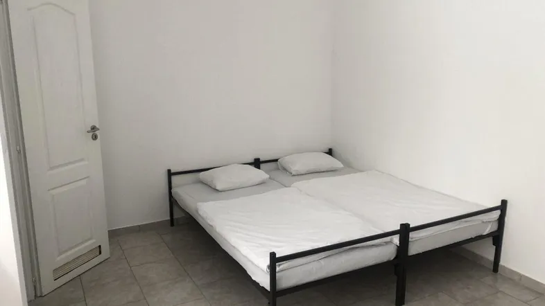 Helles Schlafzimmer mit zwei Einzelbetten, Fliesenboden und weiß gestrichenen Wänden.