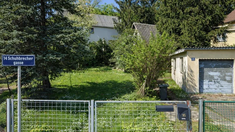 Vorgartenbereich mit alter Garage, Zaun und Straßenschild in grüner Umgebung.