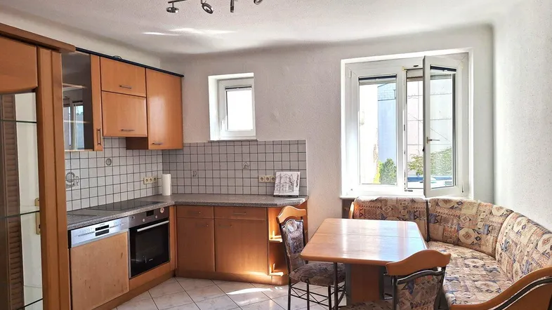 Helle Küche mit Holzeinbauschränken, Fliesenboden und integriertem Essbereich am Fenster.